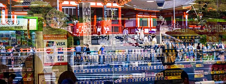 Shoppers are reflected in a window in Kyoto, Japan. Beyond the shoppers, a building is also part of the image.  