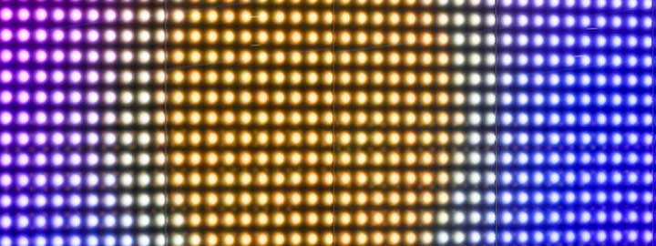 This close-up image of an LED display along Wembley Way in London shows rows of small circles of brightly colored lights. The colors form a pattern that resembles the sun at the center, surrounded by hazy glow that is, in turn, surrounded by cooler-toned lights that resemble the sky.