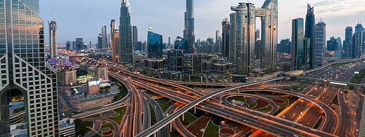 An aerial view of criss-crossing roads in Dubai. Tall buildings rise in the background.